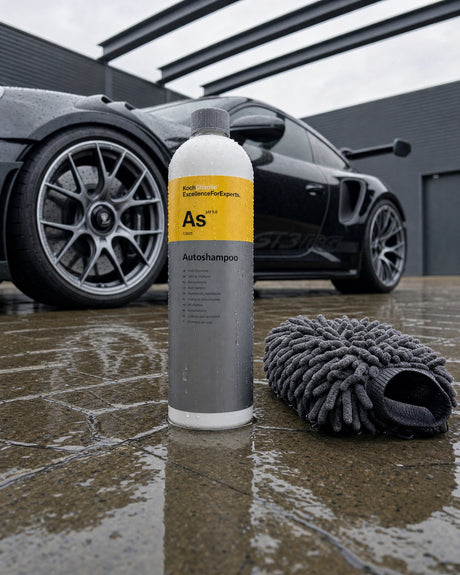 Koch-Chemie Autoshampoo „As“ steht mit Waschhandschuh auf dem nassen Pflaster vor dem sauberen schwarzen Porsche 911 GT3 RS.