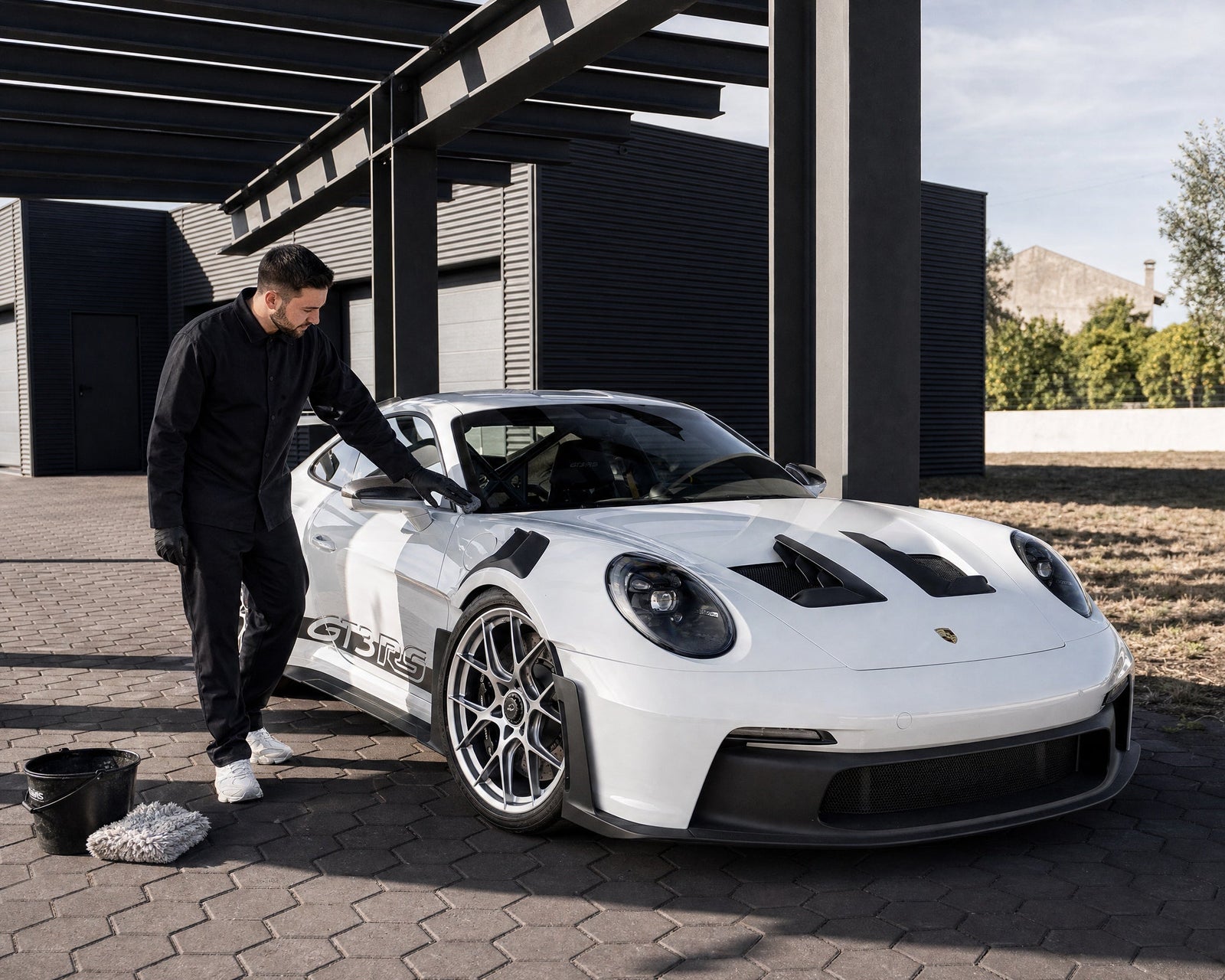 Daniel begutachtet im Schatten des Carports den Lack eines weißen Porsche 911 GT3 RS vor der Dekontamination — gezeigt im Artikel „Lack dekontaminieren im Sommer: das Schönwetterfenster nutzen“