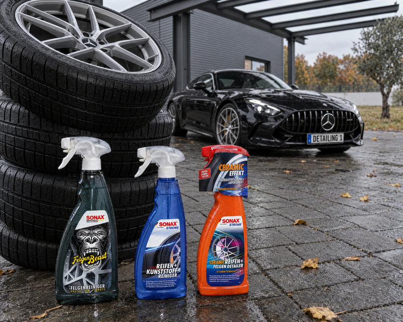 Four clean complete wheels stacked, with SONAX FelgenBeast, Tyre + Plastic Cleaner and Ceramic Detailer in front